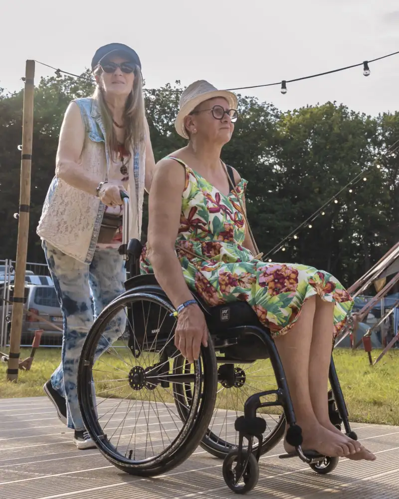 Drei Personen, davon eine im Rollstuhl, auf einem Festivalgelände