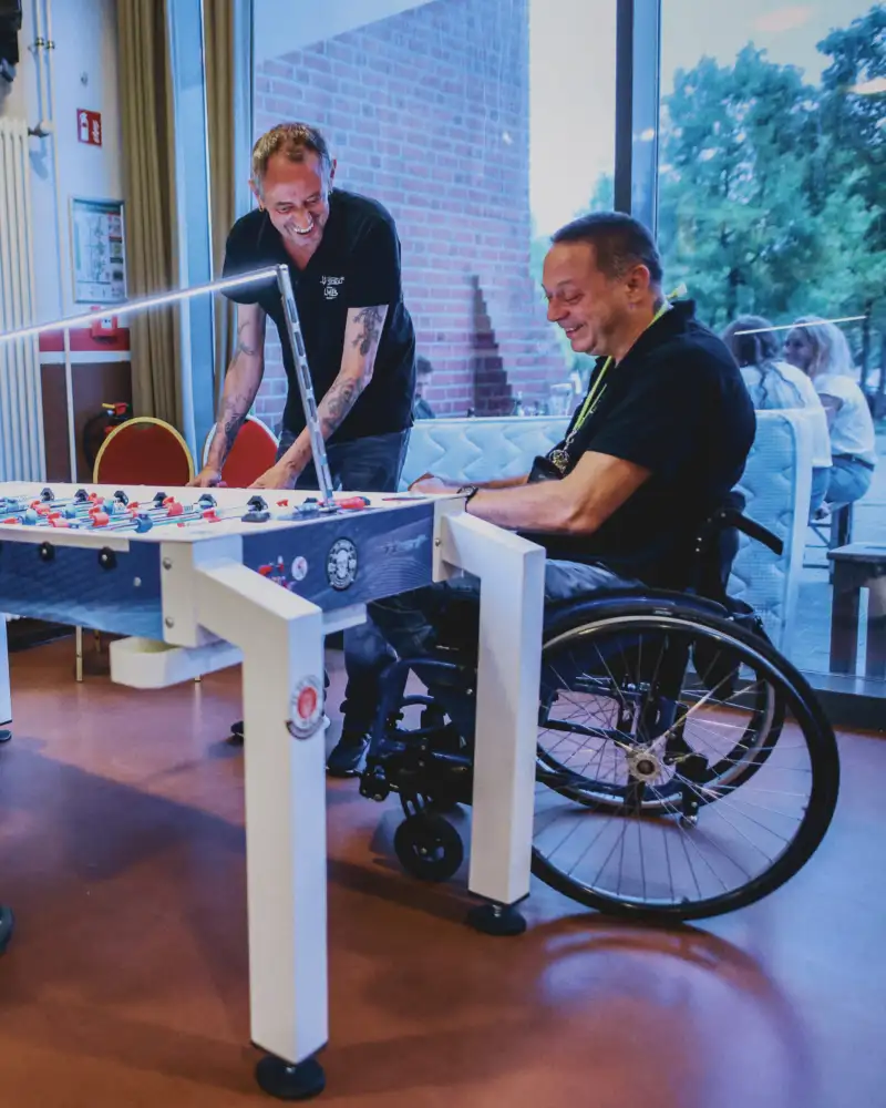 Zwei Personen beim Kickern, einer davon im Rollstuhl
