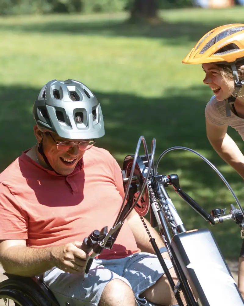 Ein Mann auf einem Handbike und eine junge Frau lachen sich an