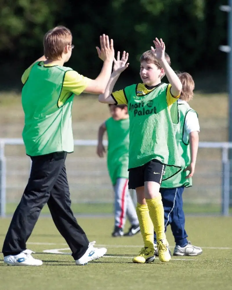 Zwei Jungen auf dem Fußballrasen klatschen sich ab. Im Hintergrund sind weitere Jungen.