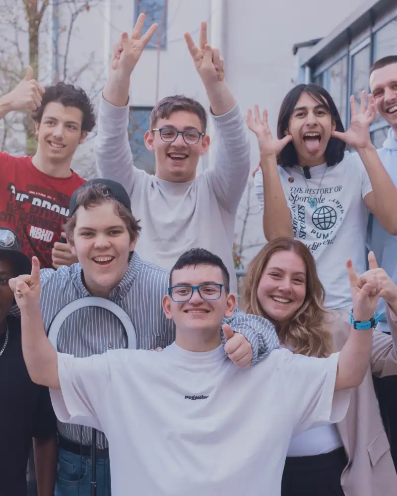 Eine Gruppe Jugendlicher schaut lächelnd in die Kamera. Die meisten heben den Daumen hoch, einer zeigt das Victory Zeichen mit gespreizten Zeige- und Mittelfingern.