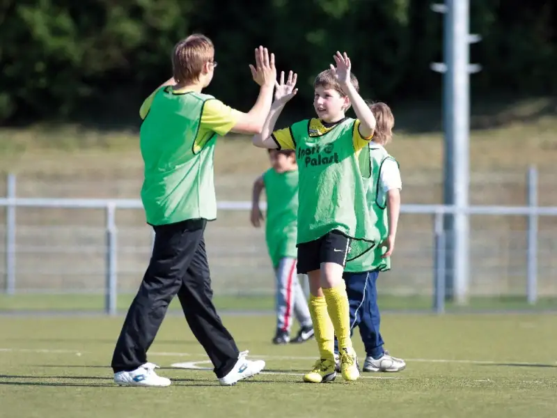 Zwei Jungen auf dem Fußballrasen klatschen sich ab. Im Hintergrund sind weitere Jungen.