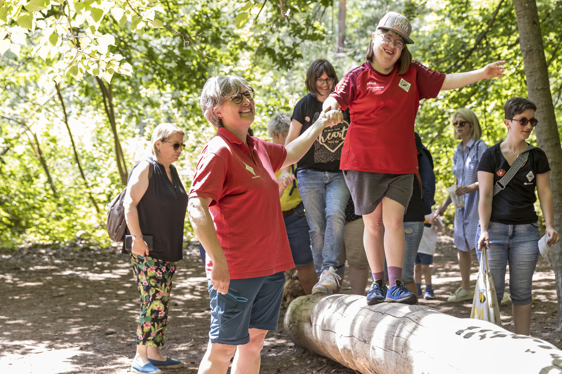 Eineinklusive Gruppe im Wald, junge Leute balancieren auf einem Baumstamm
