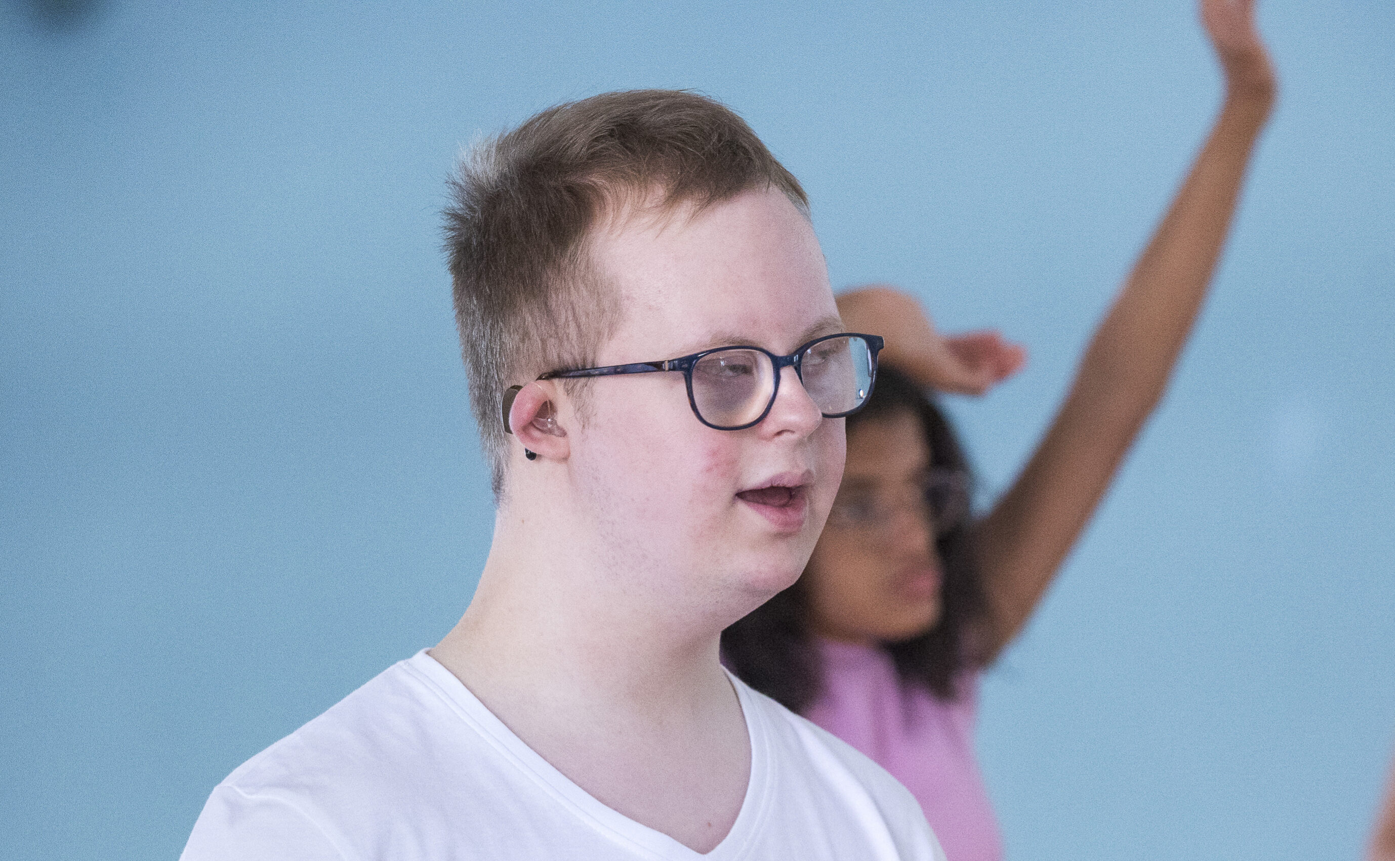 Ein junger Mann mit Downsyndrom, im Hintergrund tanzt eine junge Frau