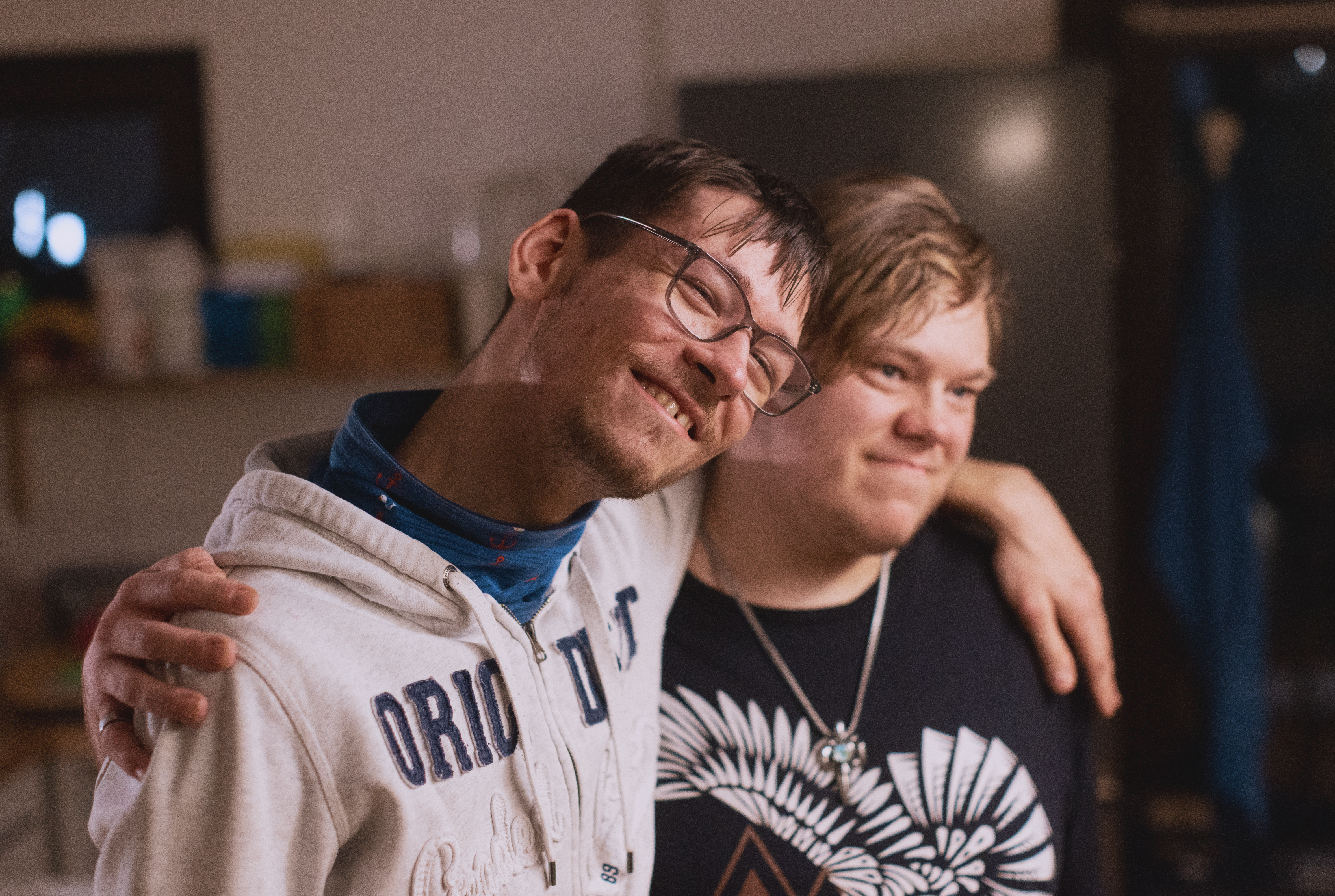 Zwei junge Männer mit geistiger Behinderung stehen lächelnd Arm in Arm nebeneinander.