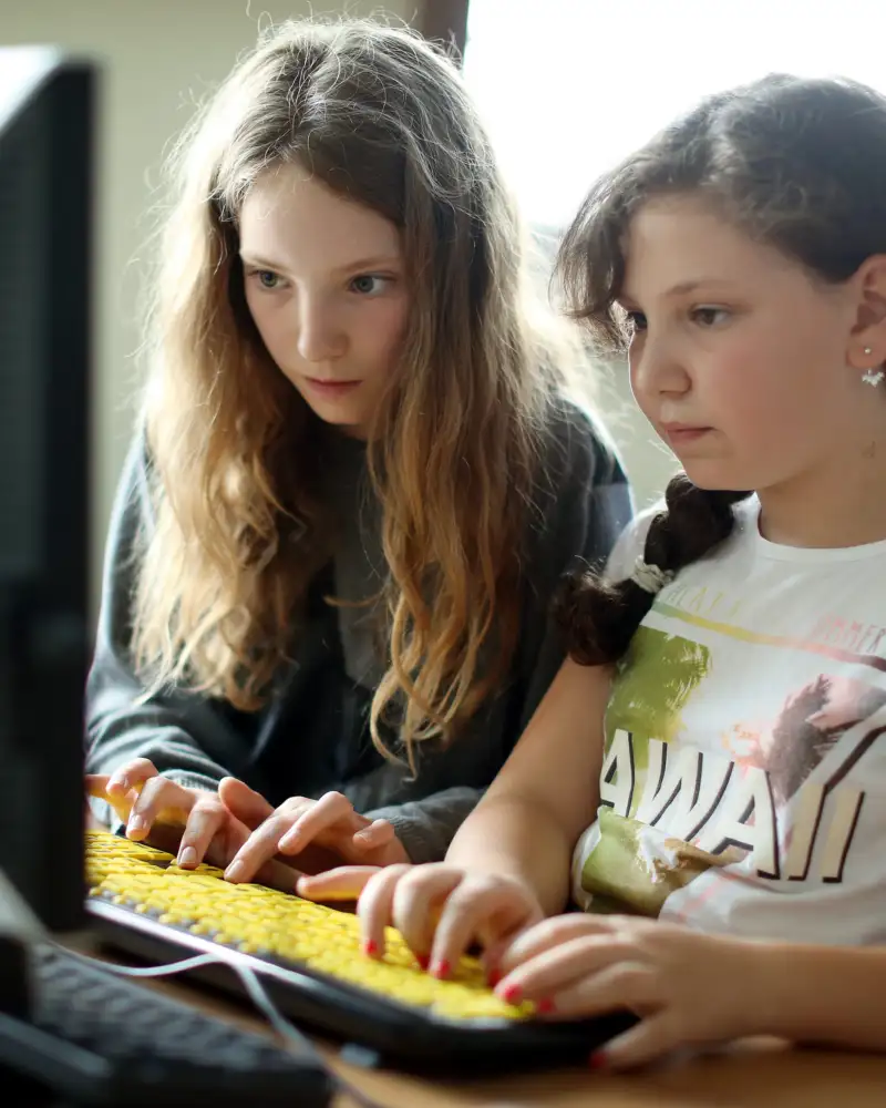 Zwei Mädchen tippen auf einer gelben Computertastatur.