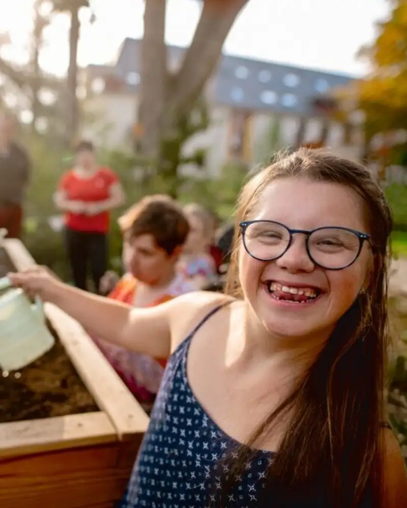 Ein Mädchen mit Downsyndrom gießt ein Hochbeet.