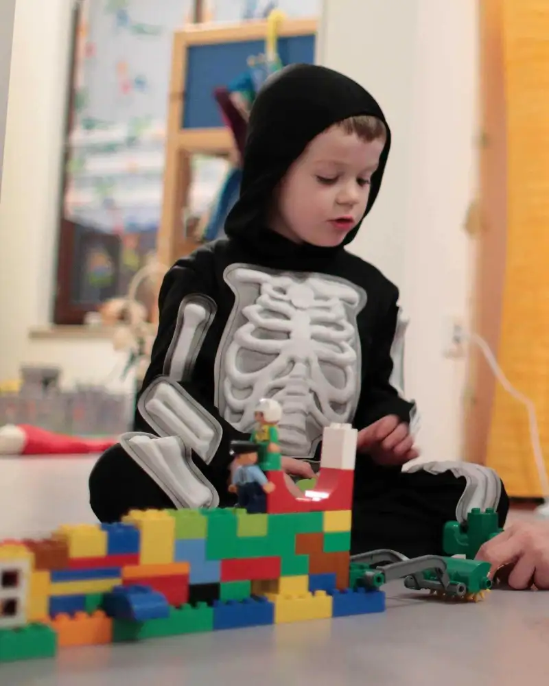 Ein kleiner Junge baut mit Legosteinen. Dabei wird er von einer Frau unterstützt.