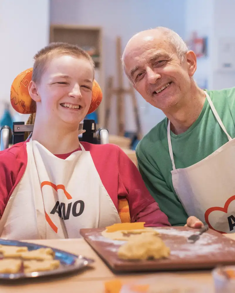 Ein junges Mädchen im Rollstuhl und sein Vater sitzen an einem Tisch, vor sich Tabletts mit selbst gebackenen Keksen.