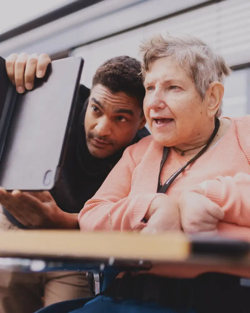 Eine Frau schaut auf ein Tablet, das ein junger Mann vor sie hält.