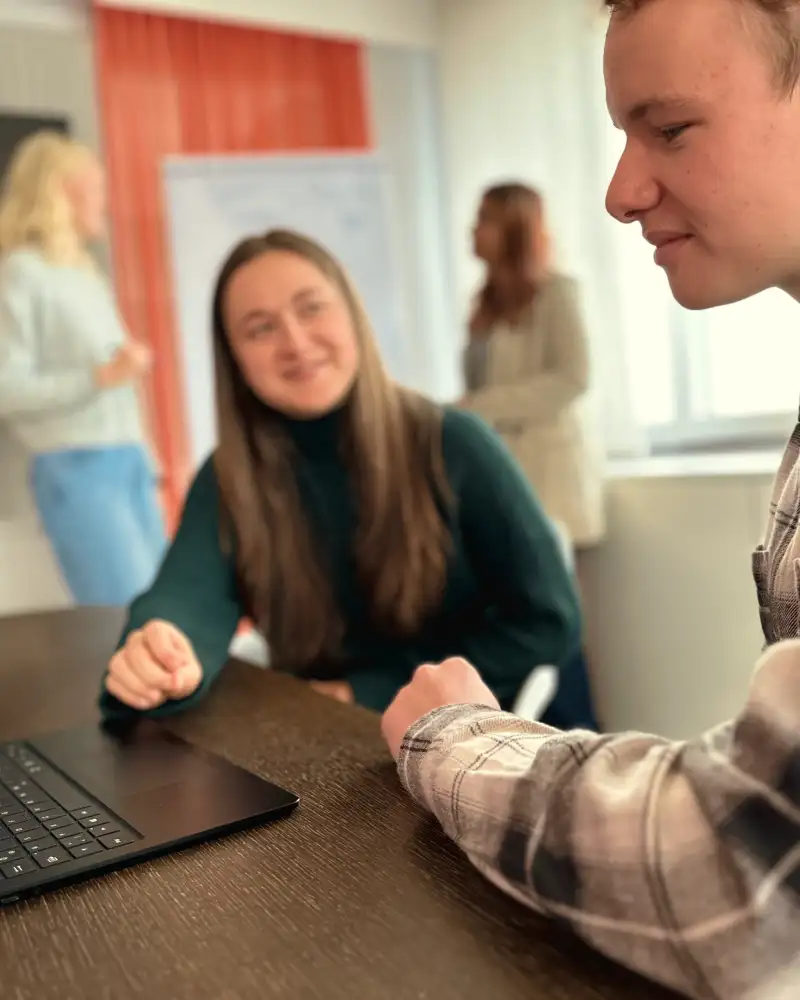 Ein Mann sitzt vor einem aufkelappten Laptop. Neben ihm sitzt eine junge Frau, die aufmunternd auf ihn schaut.