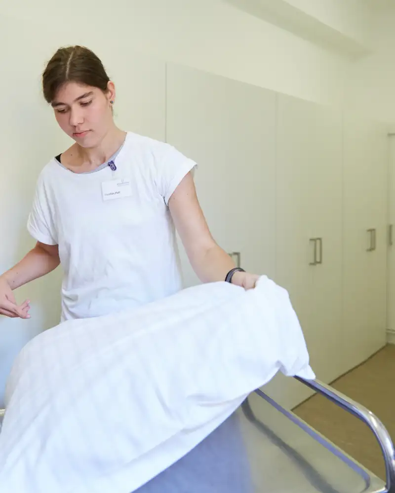 Eine Frau wechselt die Bettwäsche an einem Bett.