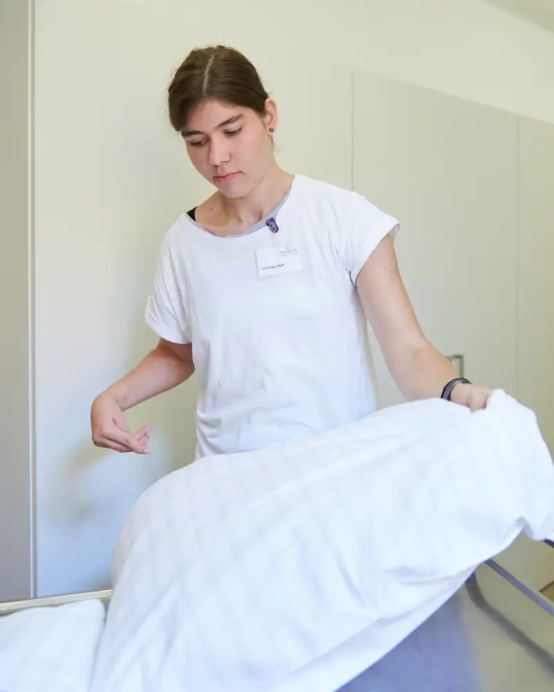 Eine Frau wechselt die Bettwäsche an einem Bett.