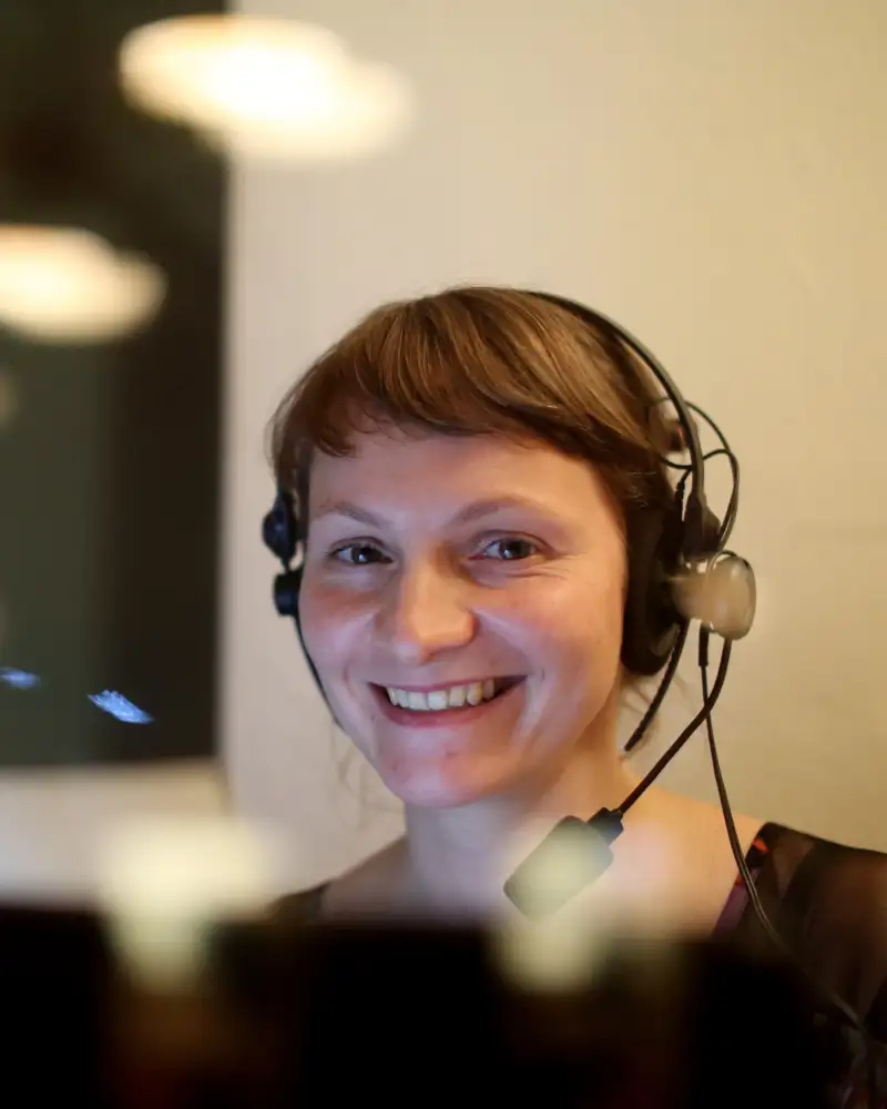 Eine Frau mit kurzem dunklen Haar trägt ein Headset und lächelt.