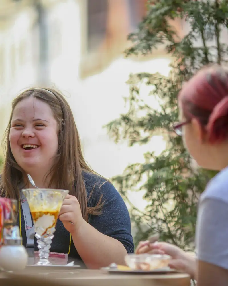 Zwei junge Frauen sitzen zusammen in einem Straßencafé. Eine hat das Downsyndrom.