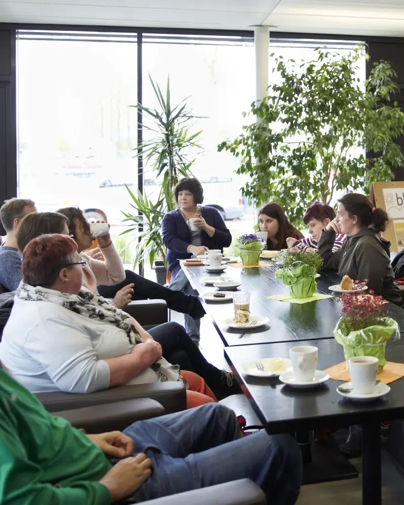 Eine Gruppe von Frauen und Männern sitzt an einem langen Tisch, der mit Tellern und Tassen gedeckt ist.