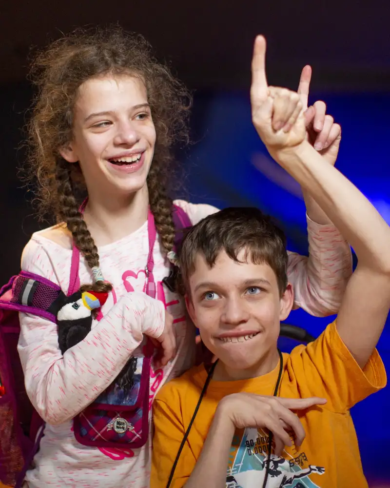 Ein kleiner Jungen mit seiner Schwester. Beide halten einen Arm in die Höhe und lächeln.