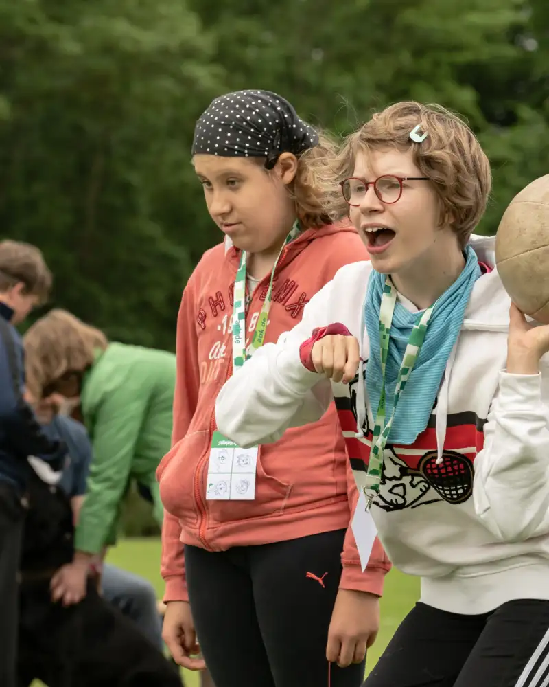 Zwei Mädchen auf einem Sportplatz. Eine von beiden wirft einen Ball.