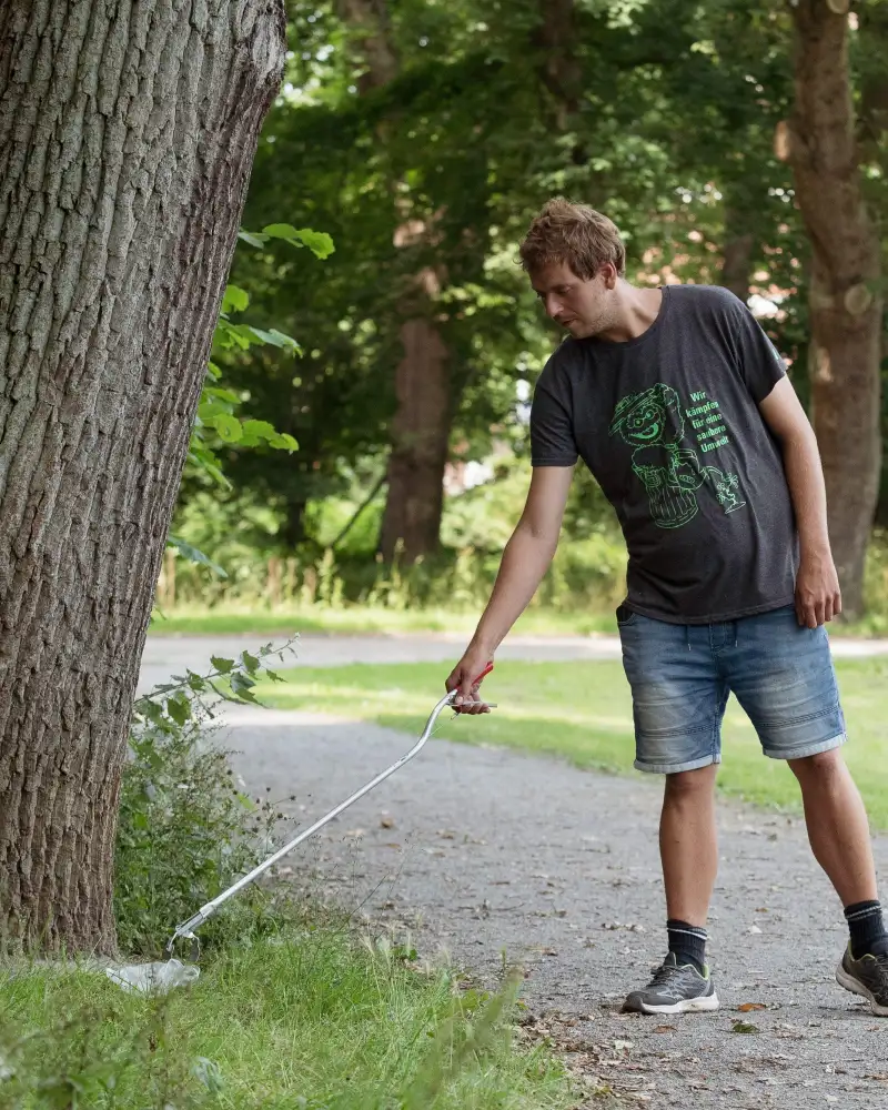 Ein junger Mann klaubt Müll in einem Park auf.