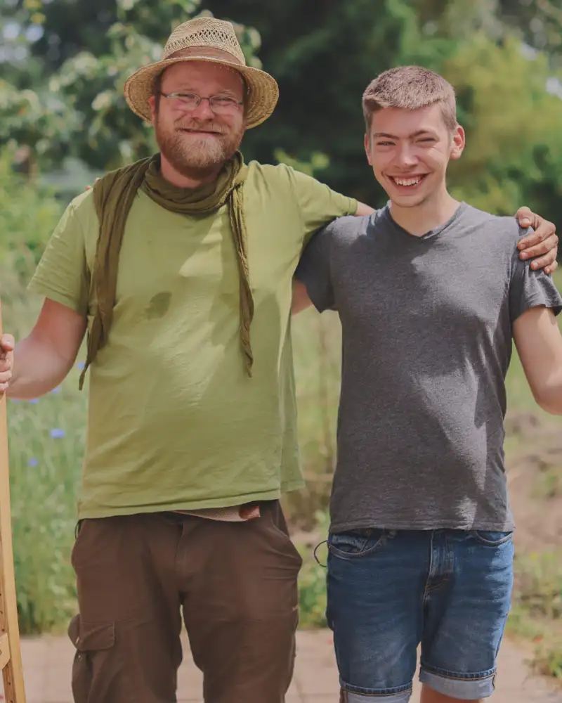 Zwei Männer in einem Garten. Der Ältere trägt einen Strohhut.
