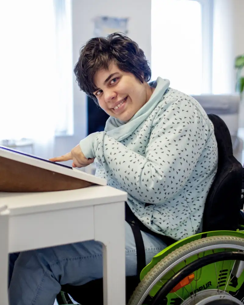 Eine Frau sitzt im Rollstuhl an einem Tisch.