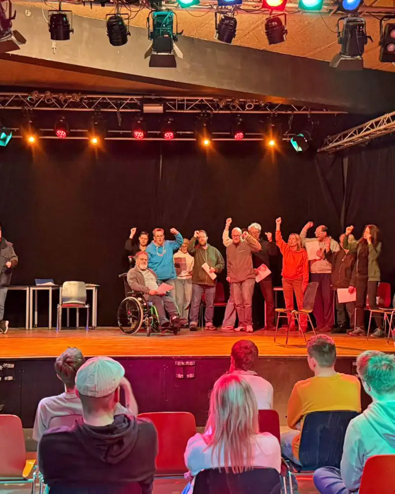 Eine Gruppe von Menschen auf einer Theaterbühne vor Publikum