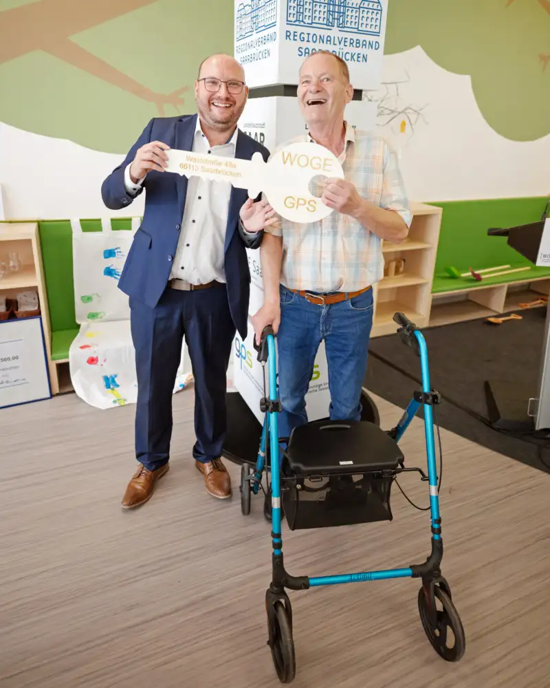 Ein Mann mit Rollator und ein anderer Mann halten ein großes Bild eines Schlüssels hoch