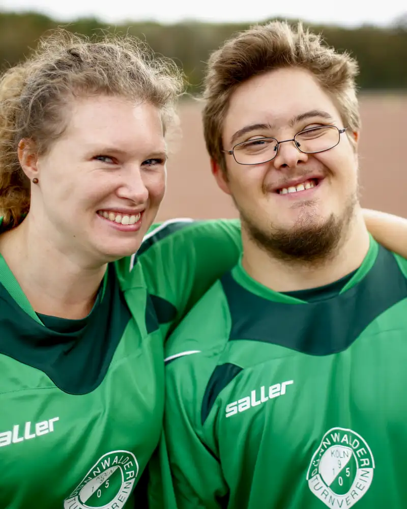 Ein junger Mann und eine junge Frau auf dem Sportplatz. Sie hat den Arm um ihn gelegt. Beide tragen Sportkleidung.