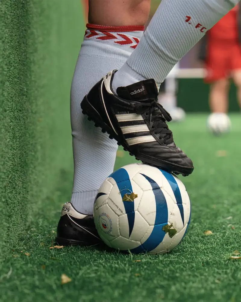 Eine Person, von der man nur die Füße und Unterschenkel sieht, stoppt einen Fußball mit dem rechten Fuß.