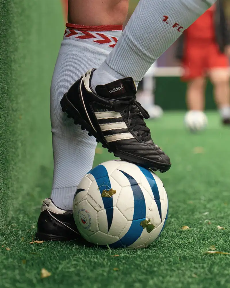 Eine Person, von der man nur die Füße und Unterschenkel sieht, stoppt einen Fußball mit dem rechten Fuß.