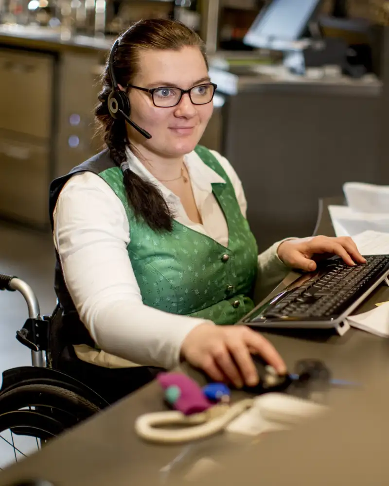 Eine Frau sitzt mit Kopfhörern an einem Schreibtisch vor einem Computer.