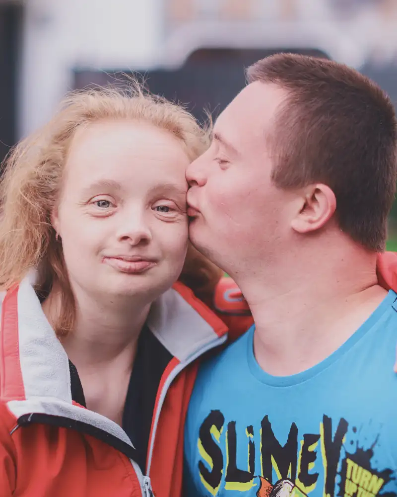 Ein junger Mann mit Downsyndrom küsst eine junge Frau mit Downsyndrom auf die Stirn