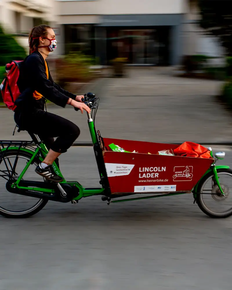 Eine Person mit Mundschutz fährt auf einem Lastenrad