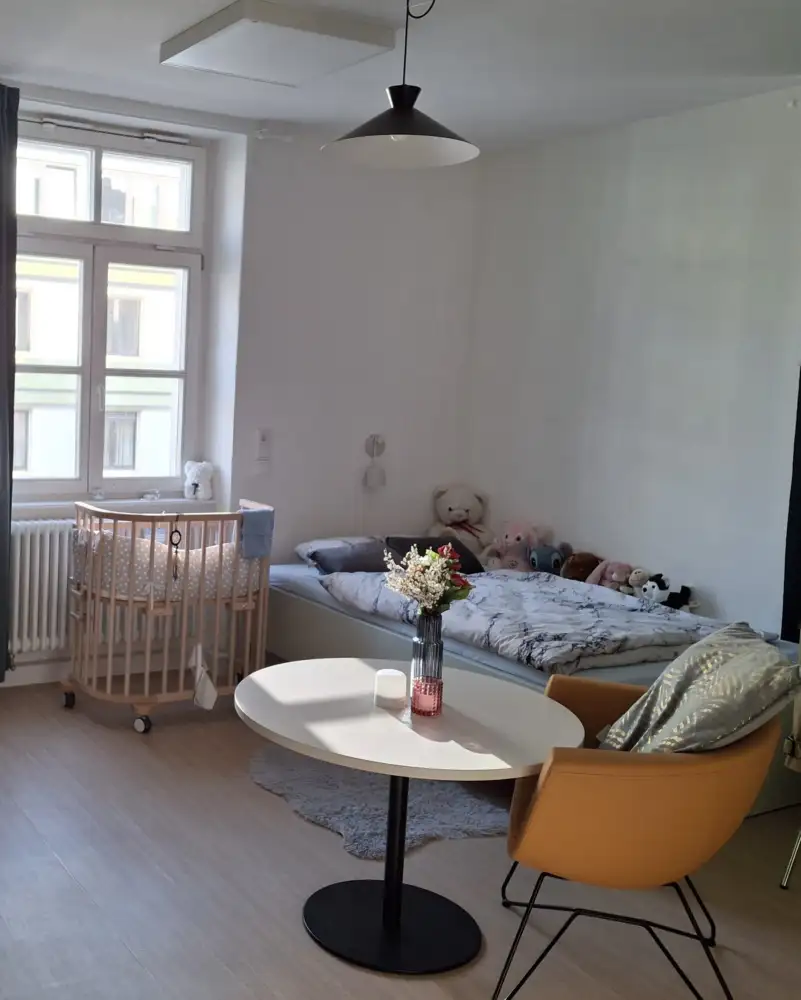 Ein Zimmer mit Kinder- und Erwachsenenbett, rundem Tisch und Sessel.