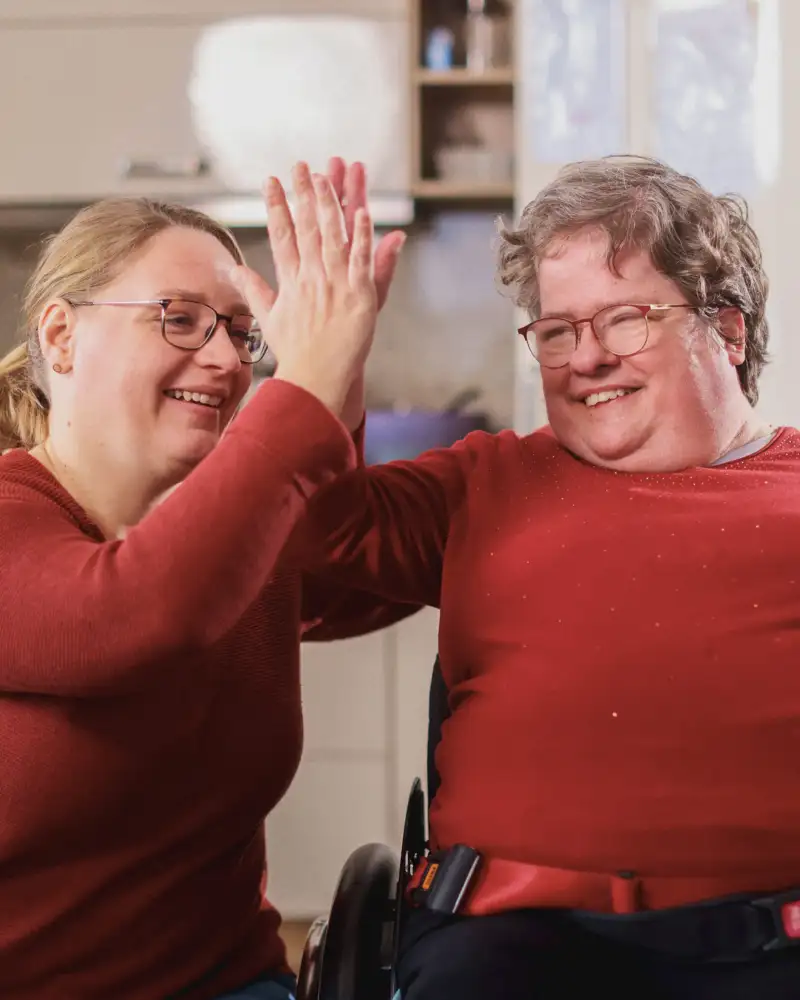 Eine Frau gibt einer anderen Frau im Rollstuhl High Five
