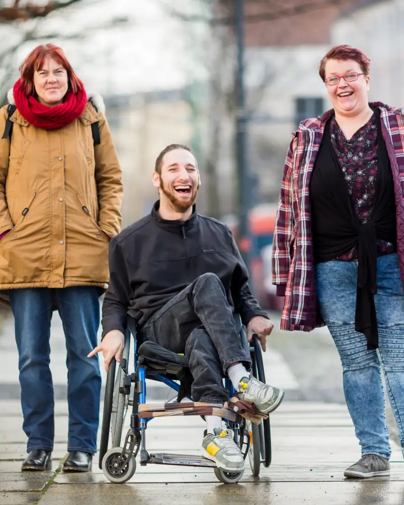 Ein Mann im Rollstuhl und zwei Frauen sind unterwegs in der Stadt.