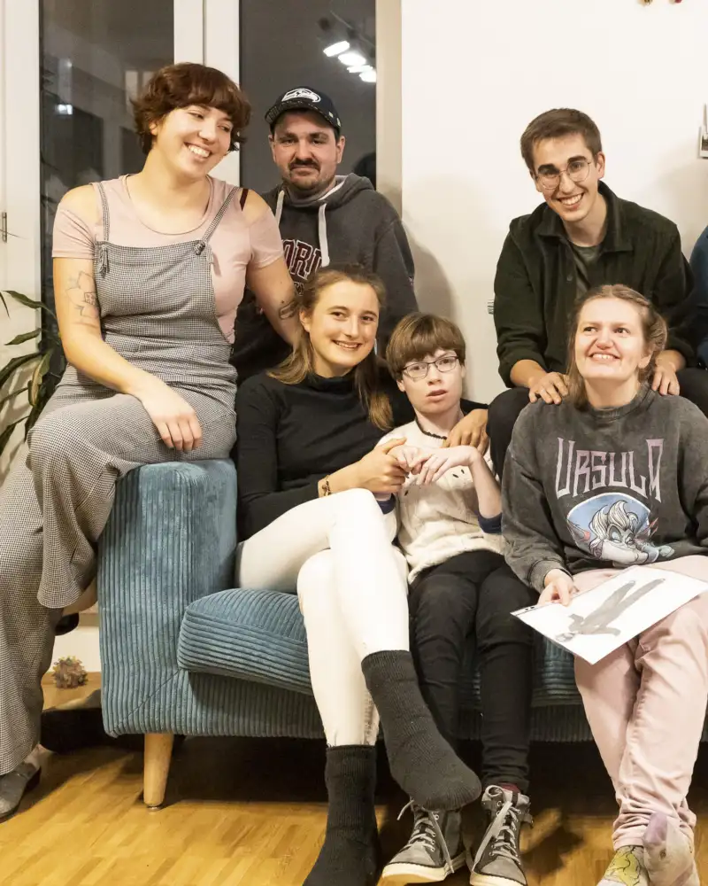 Eine Gruppe von Menschen mit und ohne Behinderung sitzt auf einem Sofa zusammen.