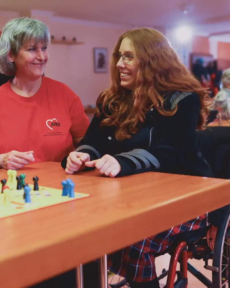 Drei Frauen spielen miteinander Mensch ärgere dich nicht. Eine von ihnen sitzt im Rollstuhl.