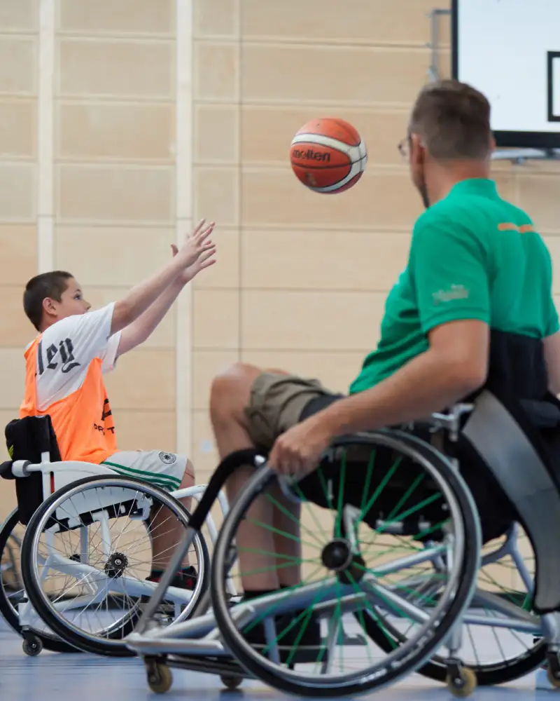 Ein Junge im Rollstuhl wirft einen Basketball zum Netz