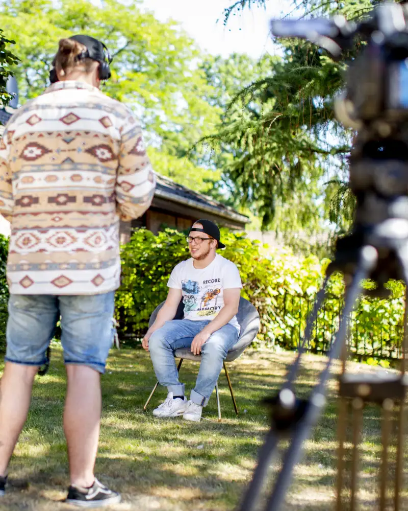 In einem Garten findet ein gefilmtes ein Interview mit einem Jugendlichen statt.