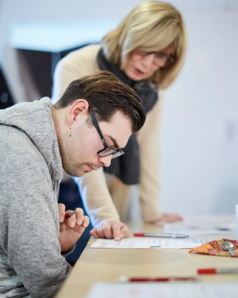 Eine Frau beugt sich über einen jungen Mann, der in einem Schriftstück liest.