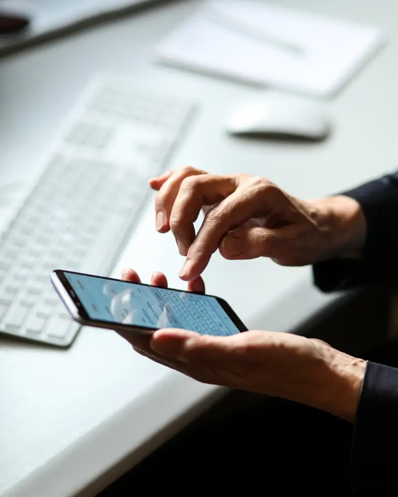 Eine Person, von der nur die Hände zu sehen sind, tippt auf ein Mobiltelefon. Daneben liegt eine Computertastatur.