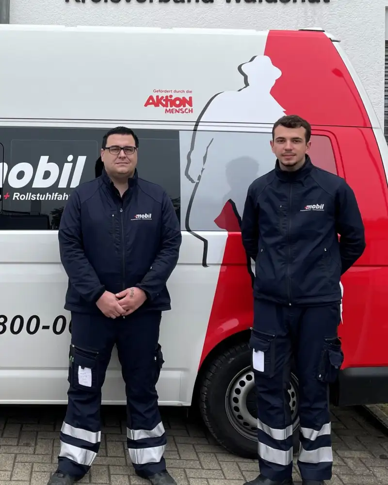 Zwei Männer in blauen Uniformen stehen vor einem Mercedes Sprinter des DRK.