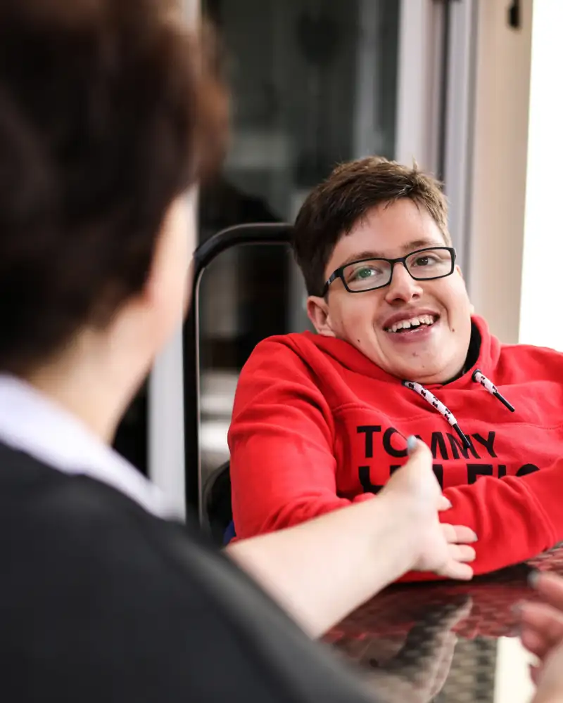 Eine Frau spricht mit einem jungen Mann im Rollstuhl, der ihr gegenüber sitzt.