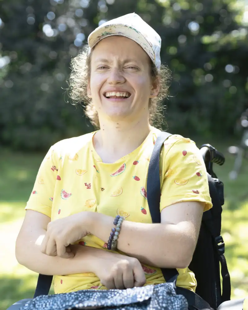 Eine Frau sitzt im Garten in einem Rollstuhl und lacht.