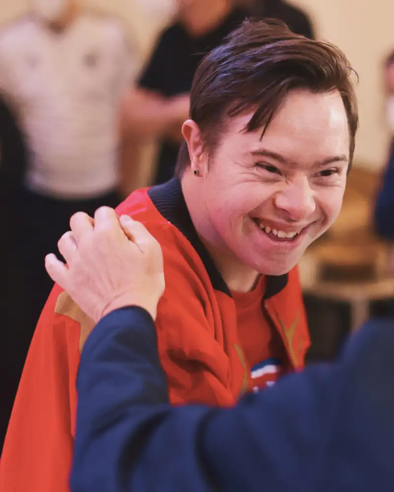 Ein junger Mann mit Downsyndrom steht lachend in einer Gruppe Leute