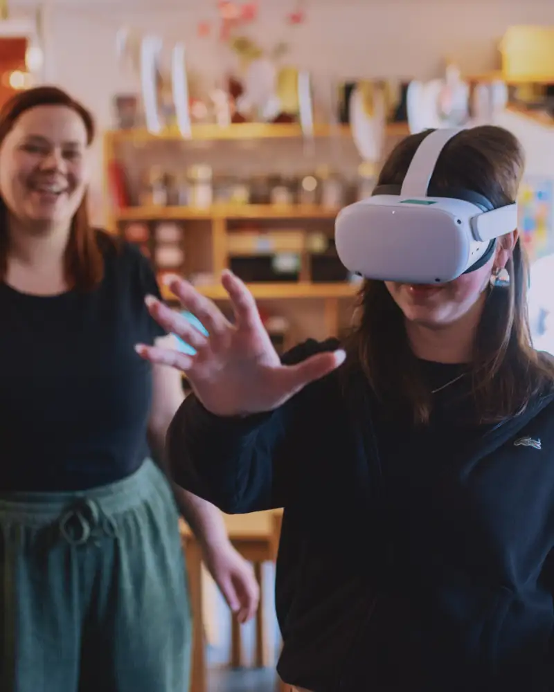 Ein Mädchen mit VR Brille, im Hintergrund steht eine lächelnde Frau