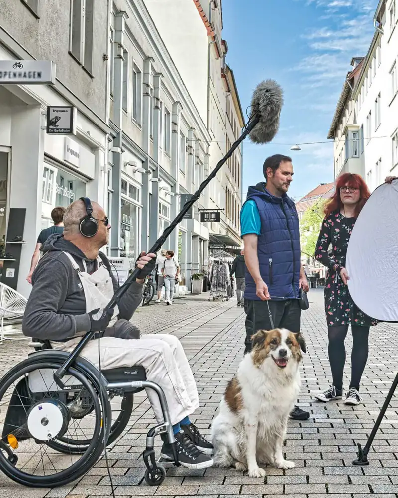 Ein Mann im Rollstuhl macht eine Tonaufnahme bei einem Interview auf einer Straße