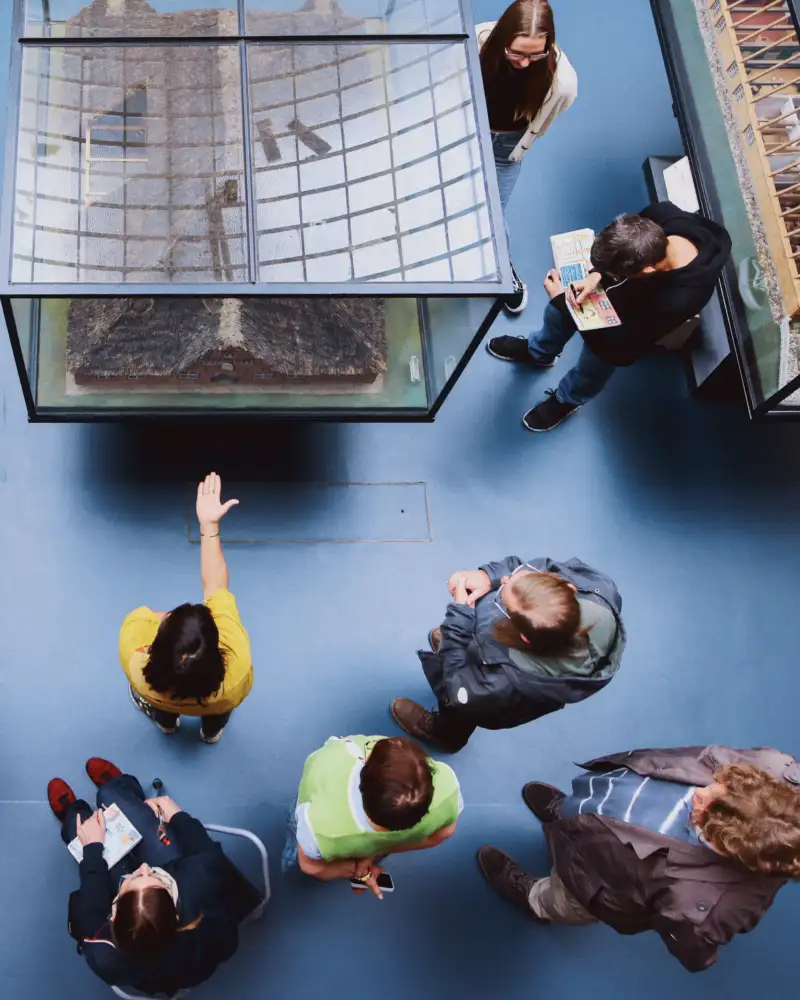 Blick von oben auf eine Gruppe Museumsbesucher*innen vor Schaukästen