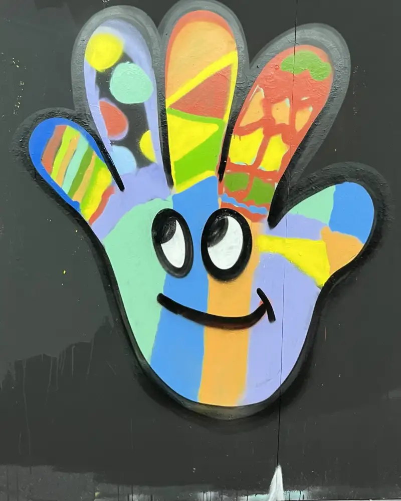 Zeichnung einer bunten Hand auf einer schwarzen Tafel. Die Handfläche hat Mund und Augen.